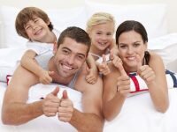 Family playing in bed with thumbs up